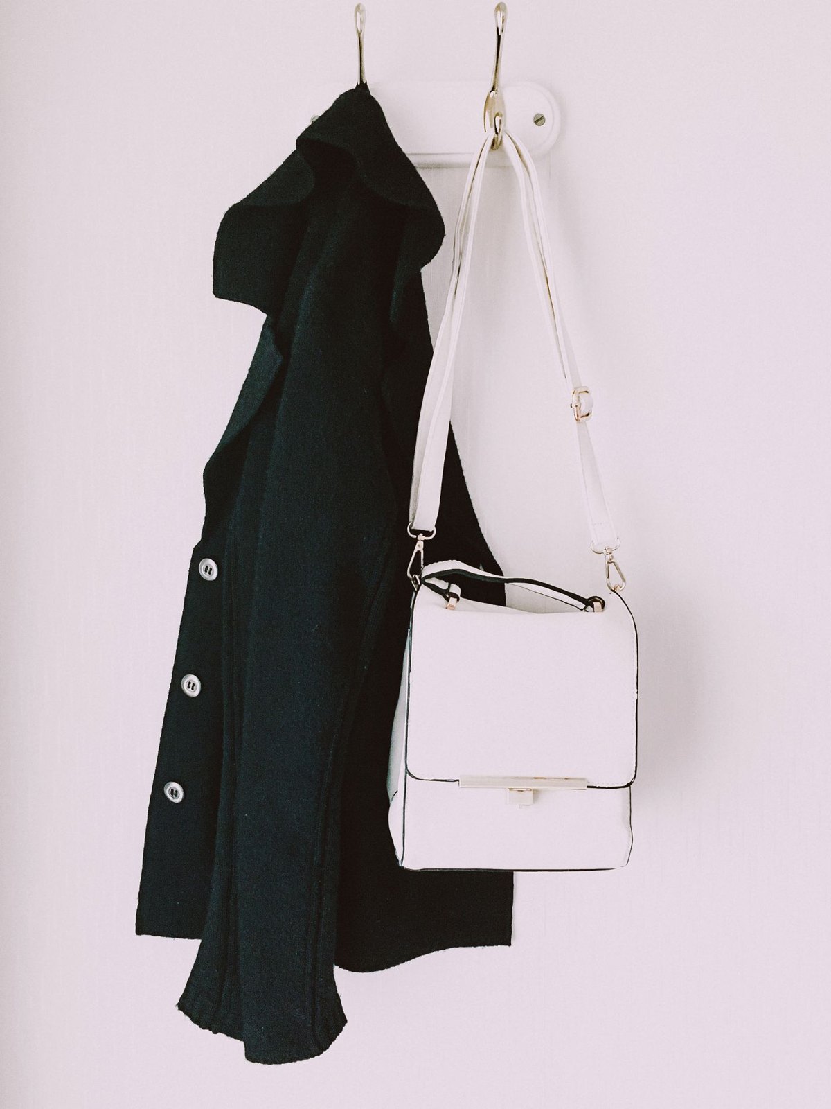 White crossbody bag hanging beside a dark coat