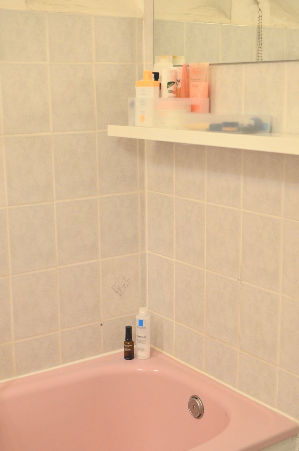Bottles arranged on a bathroom shelf beside a pink bath