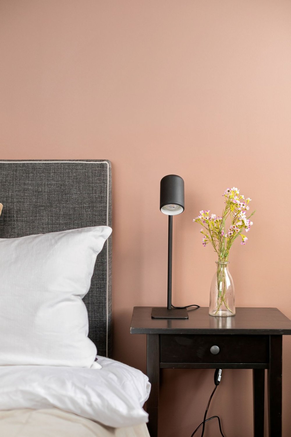 Bedside table with a lamp and flowers beside a bed