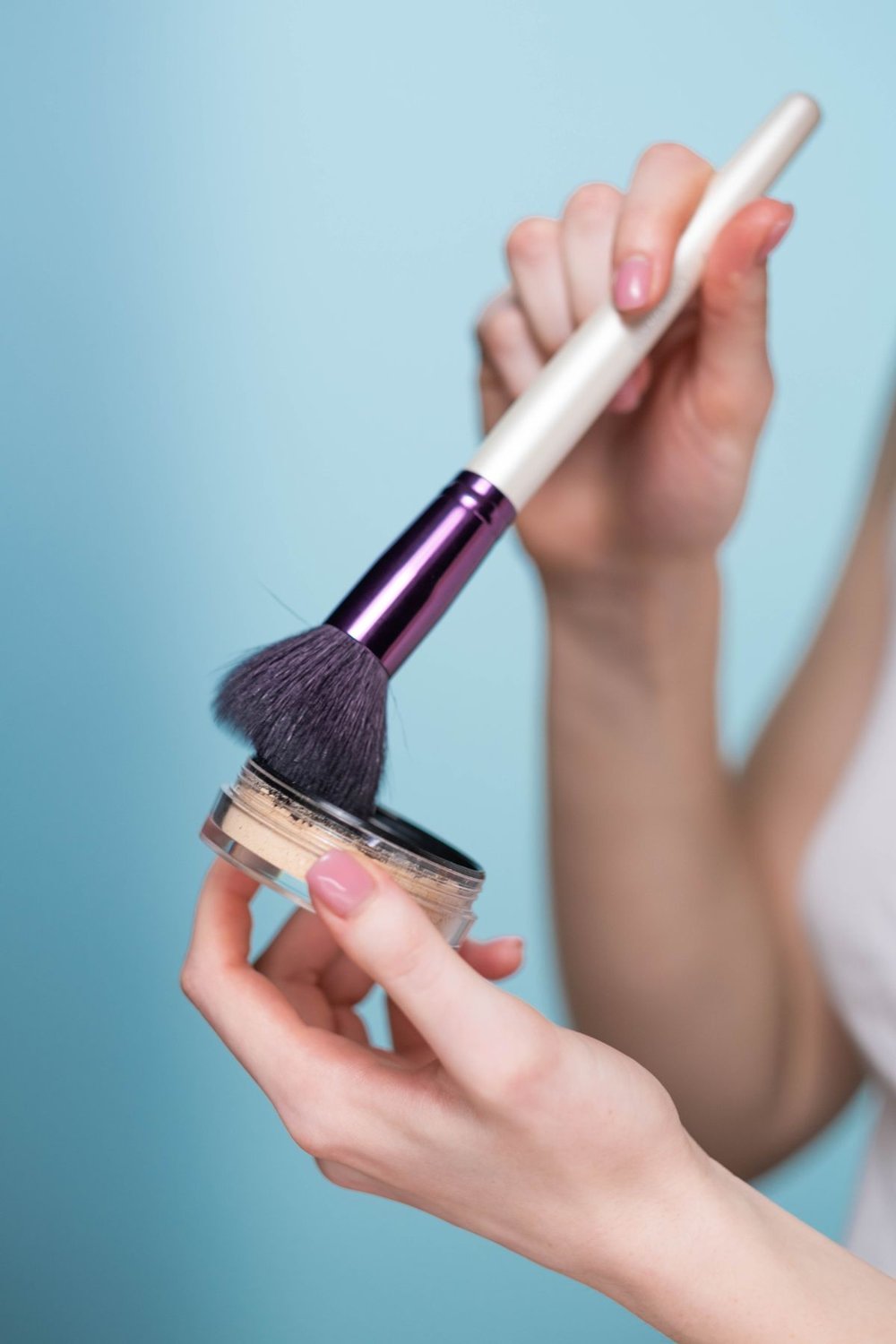 Person holding a blush compact and a makeup brush