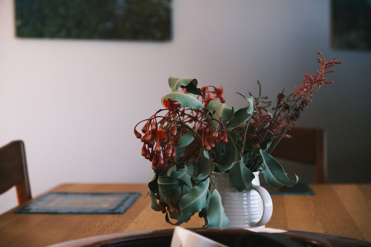Red flowers and green foliage in a ceramic vase on a wooden table