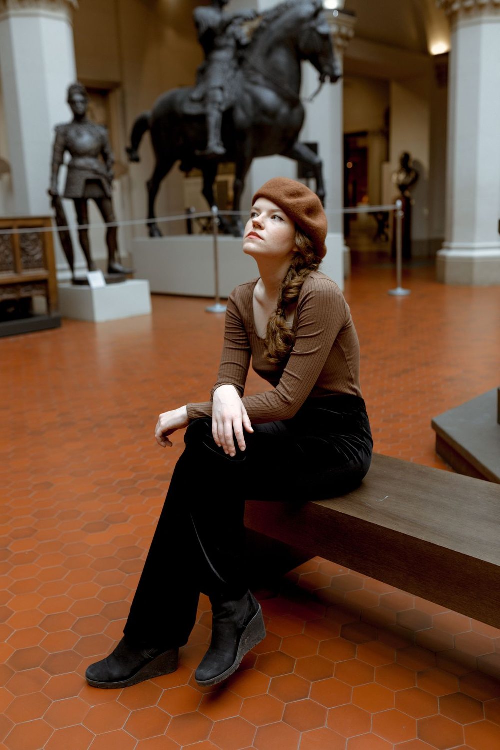 Woman in a brown sweater and black trousers seated in a museum