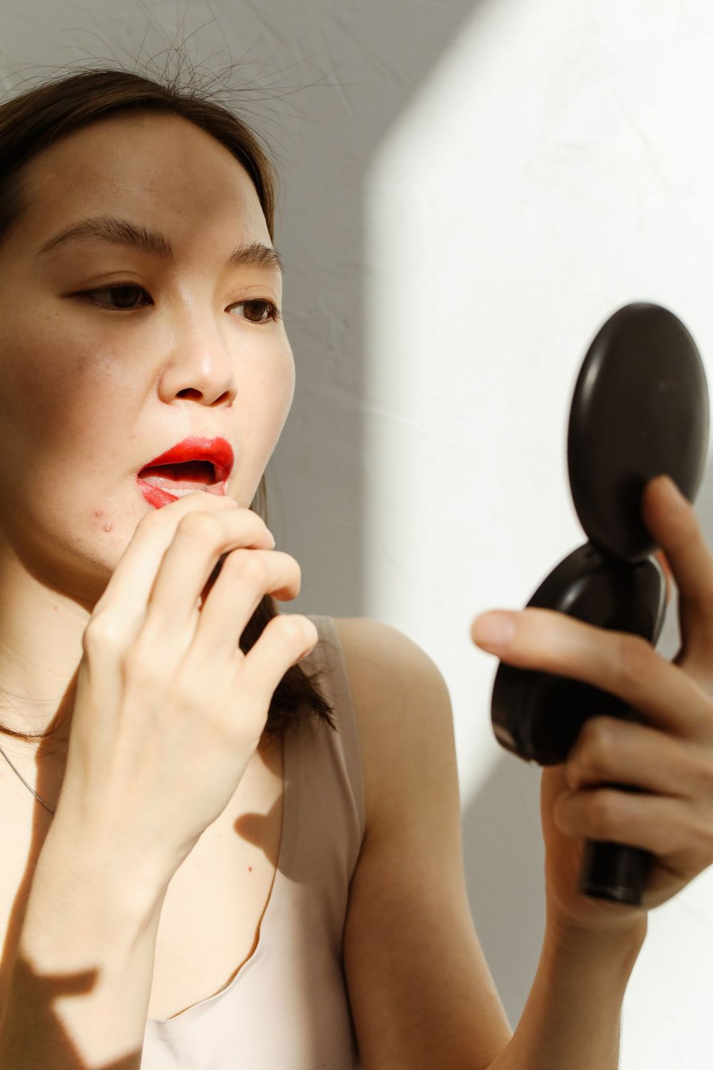 Woman applying red lipstick while looking in a small mirror
