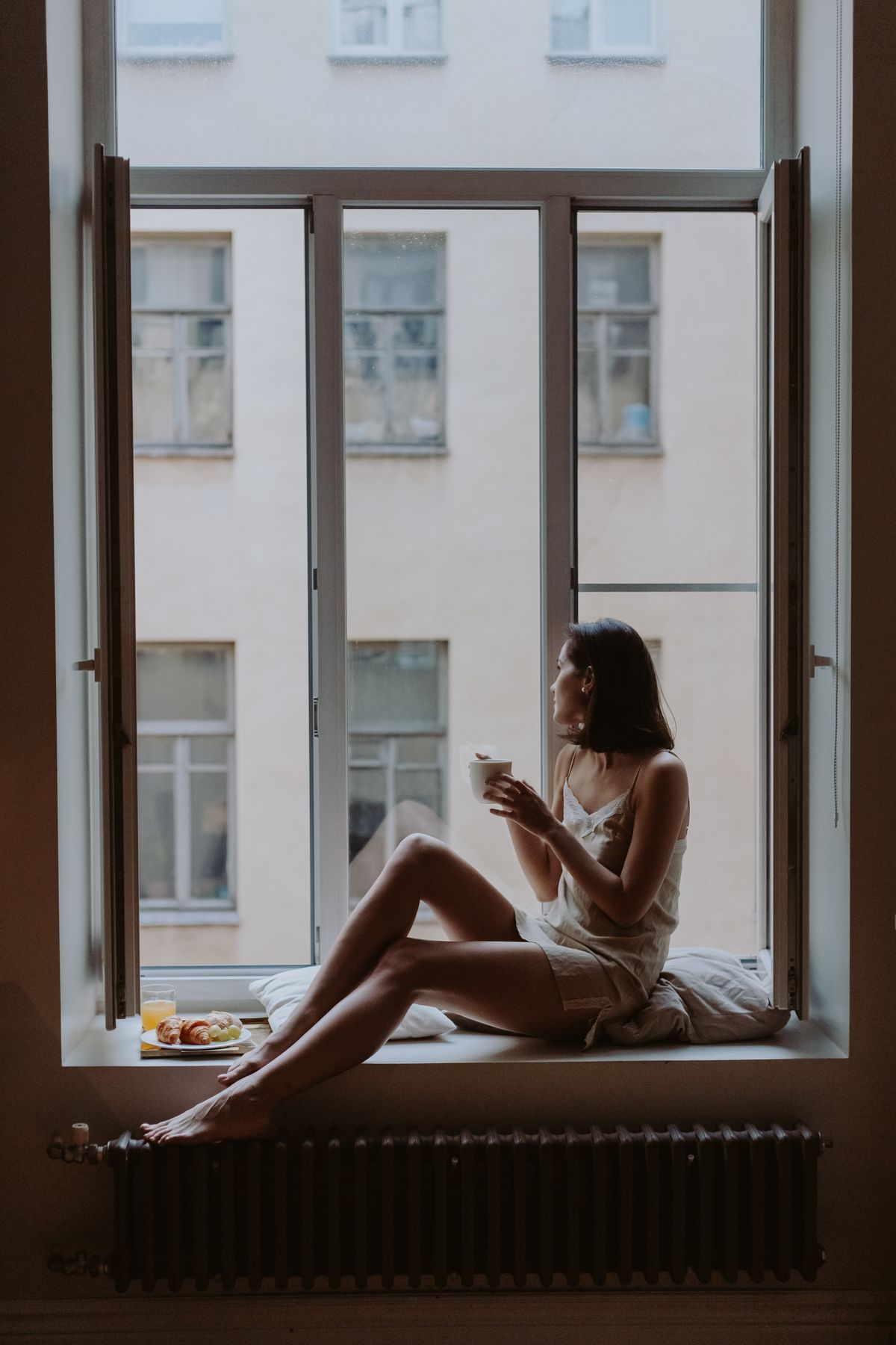 Woman with breakfast and a drink beside an open window
