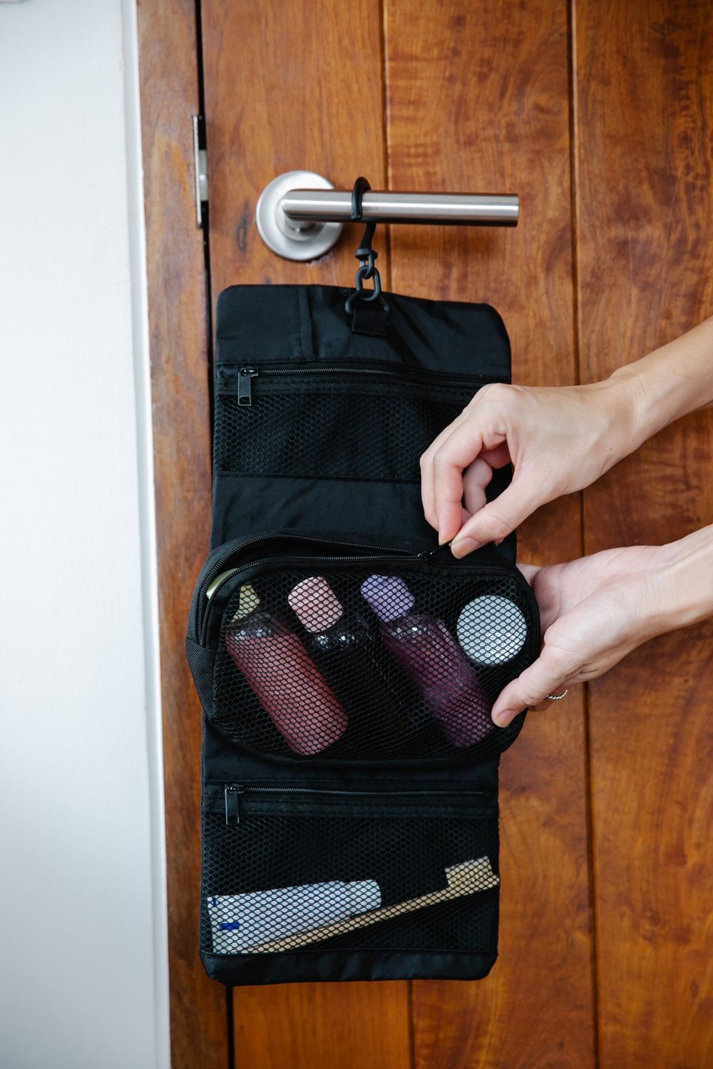 Open toiletry bag hanging from a wooden door handle
